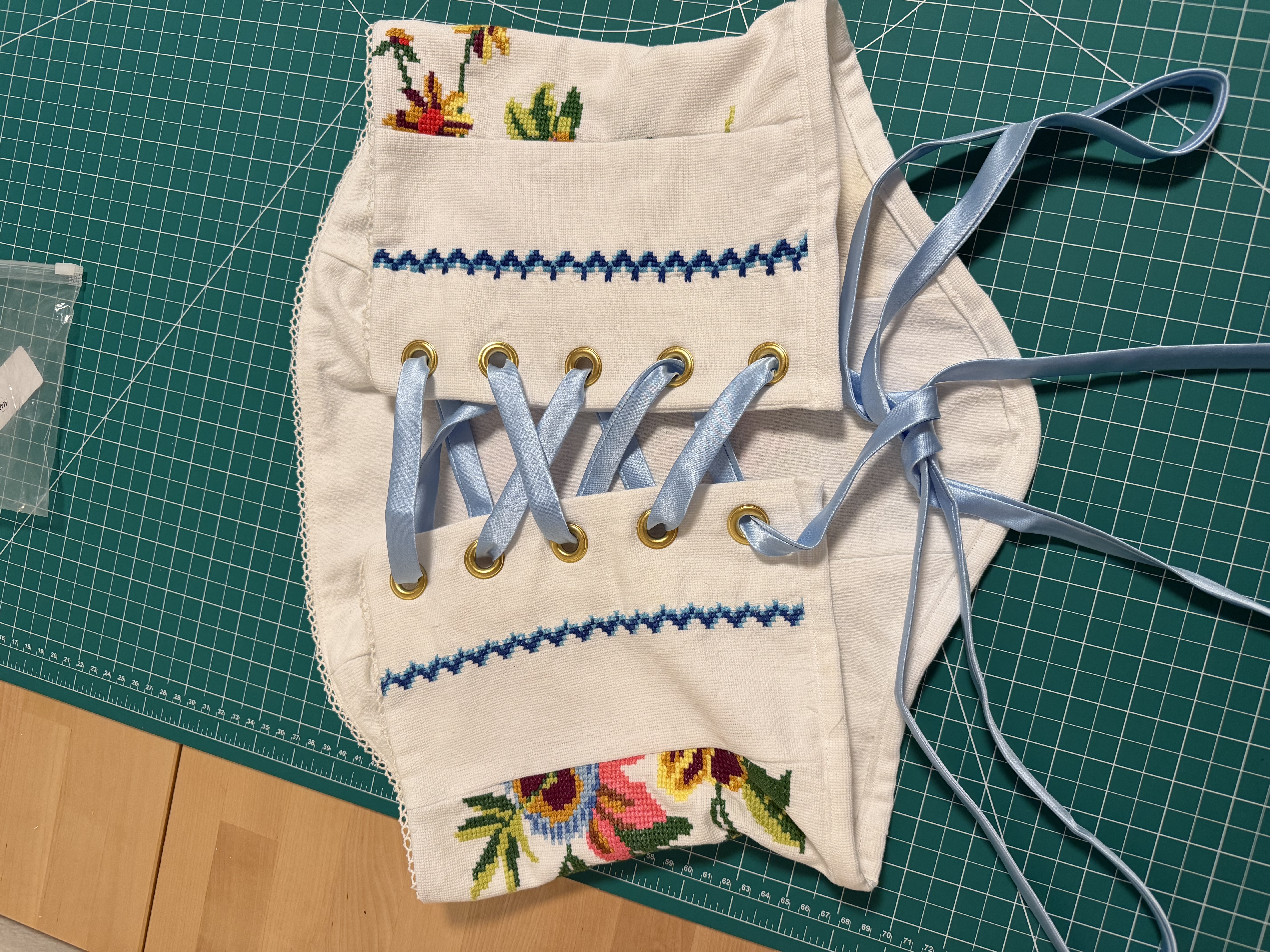 The finished corset laid flat on the cutting mat, back view, showing the grommets and light blue lacing